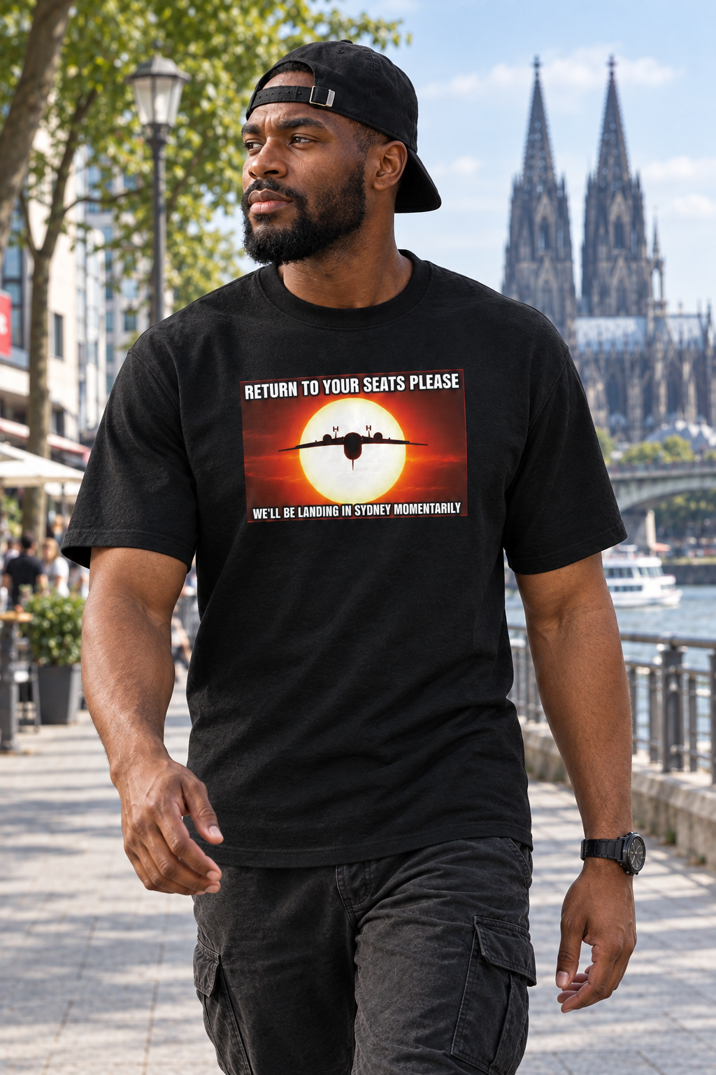 Stoere Afrikaanse man met pet achterstevoren in zwart Return to your seats T-shirt, wandelend in Keulen